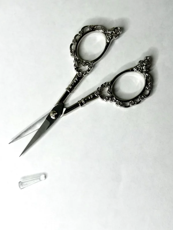 Ciseaux de précision 11 cm vintage motif floral posés sur tissu, prêts pour couture et broderie